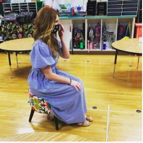 Kindergarten teacher sitting alone in an empty classroom facing a yardstick, waiting for her students to begin the end of year moving up celebration.