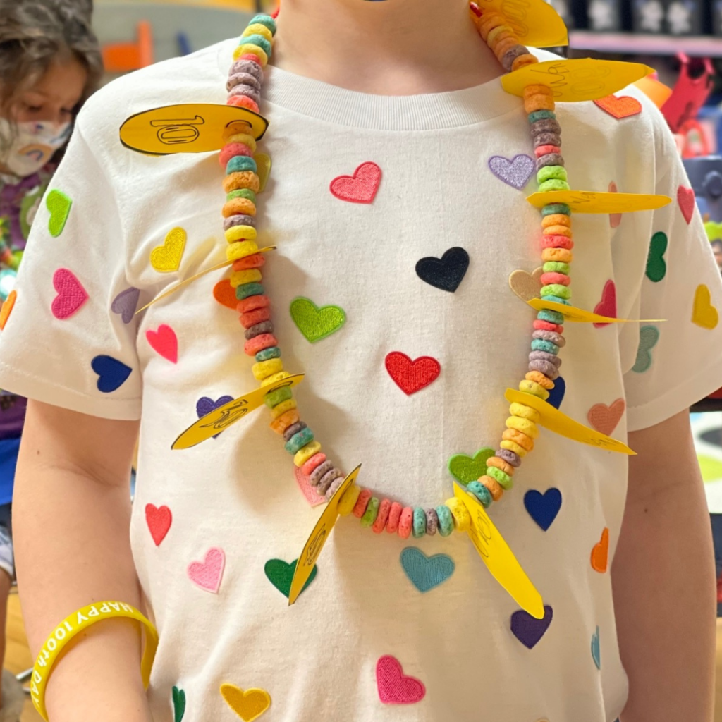 a completed 100 day fruit loop necklace on a boy with 100 hearts on his shirt