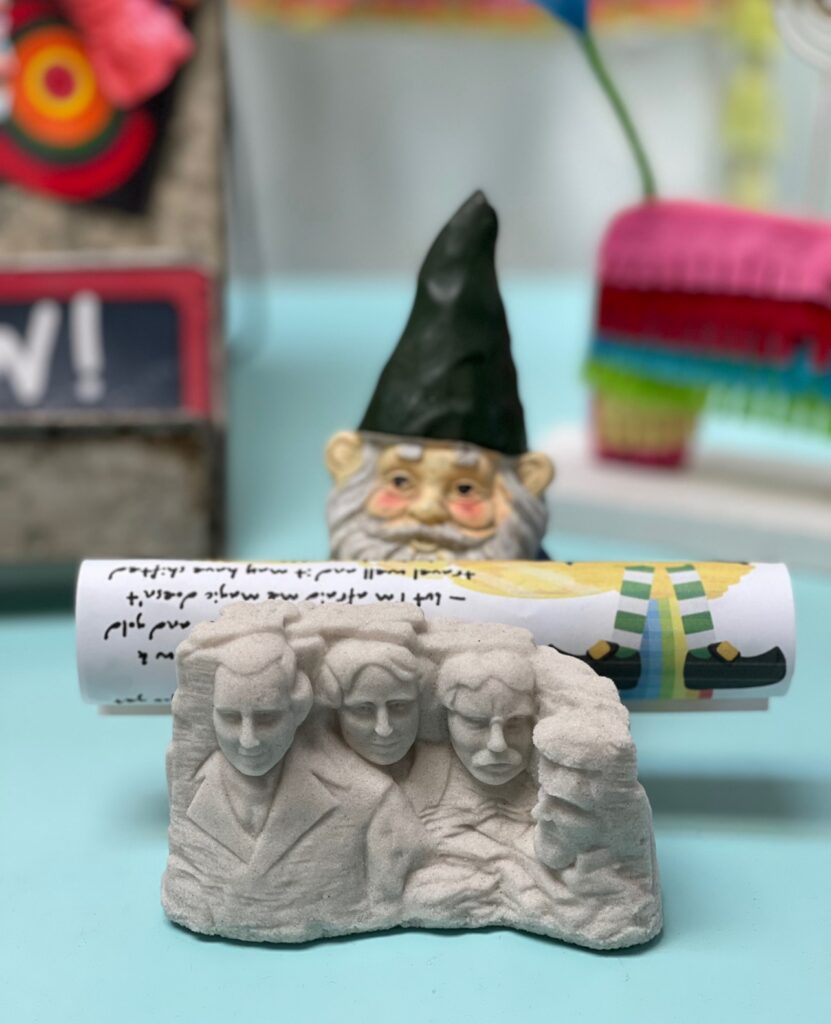 gnome in kindergarten classroom holding a special note from the visiting leprechaun - on top of a mini Mr. Rushmore