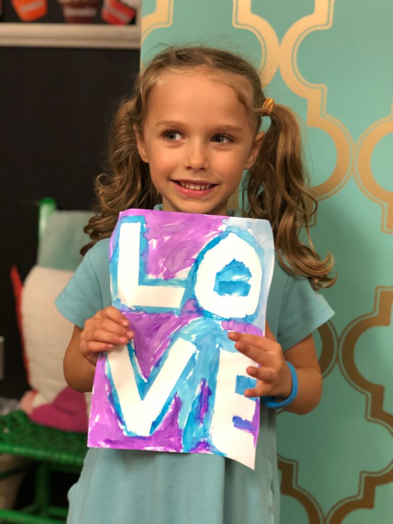 kindergartener holding a hand-painted drawing that says "love"