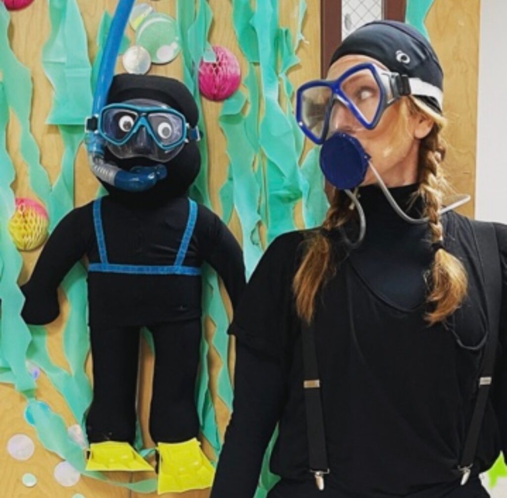 Teacher in a scuba suit looking at a doll-size scuba diver